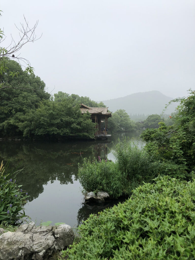 A large lake with green foliage surrounding it and a Chinese structure in the background.