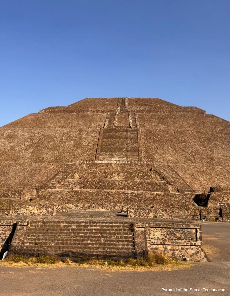 A large brown colored monument with a central staircase leading to the top against a bright blue sky.