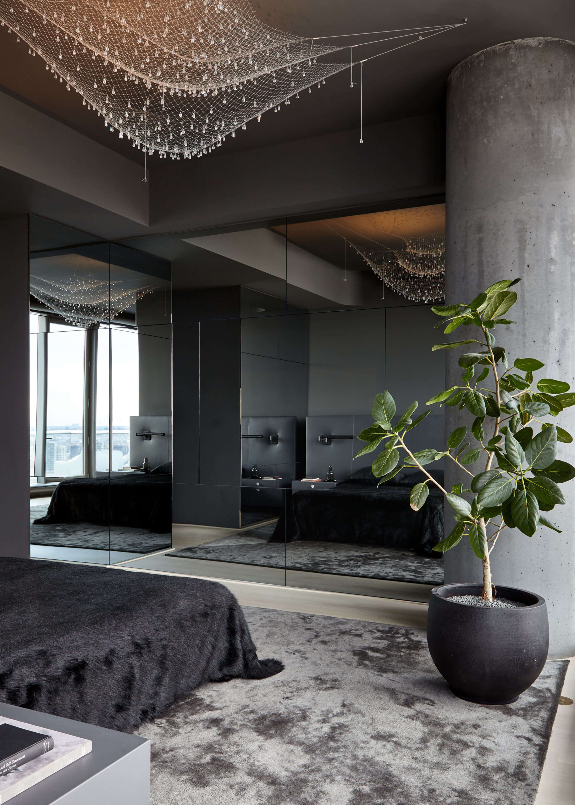 Bedroom with gray walls, gray carpet, black bedspread, mirrored wall, abstract mesh ceiling light and potted plant.