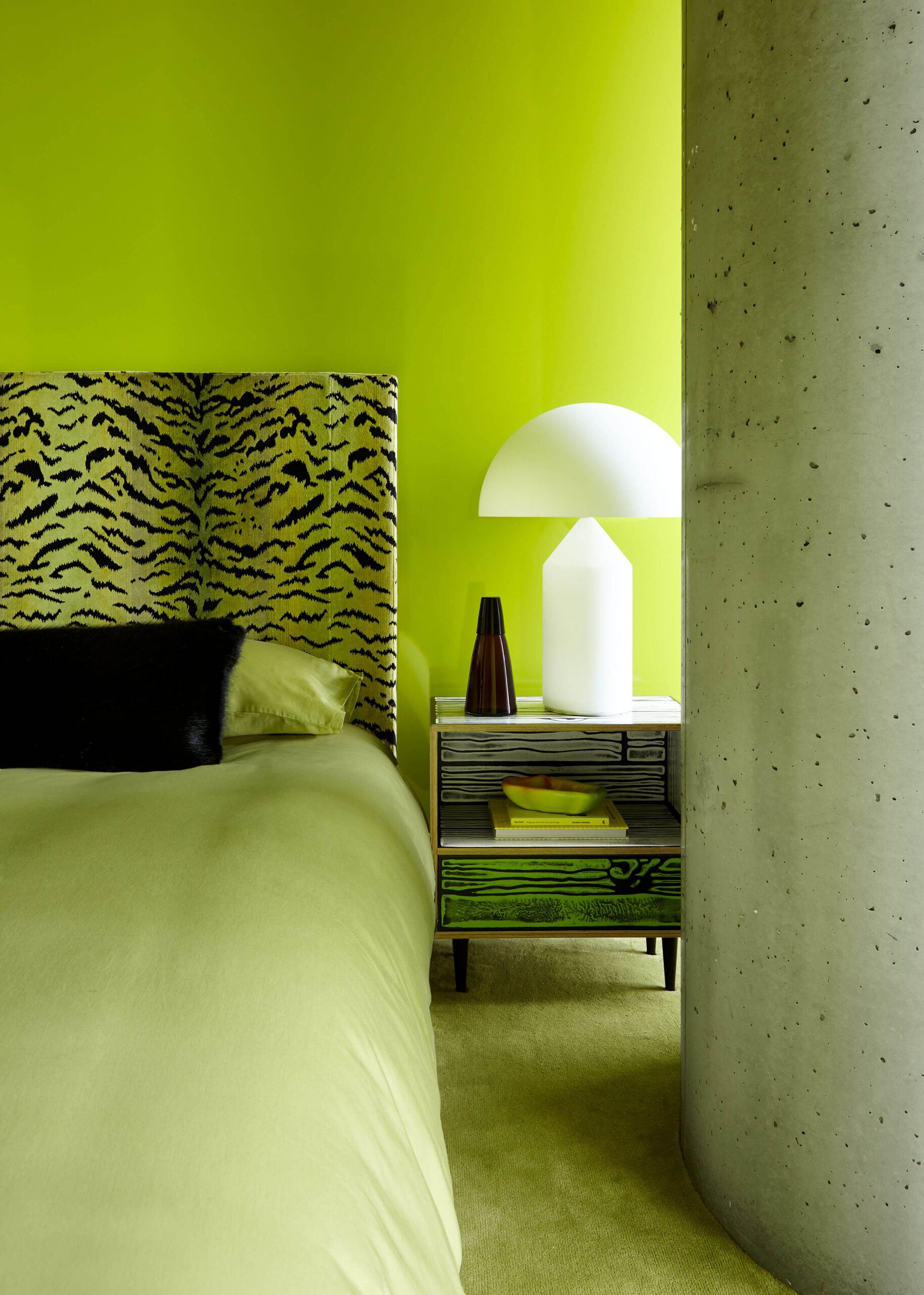 Bedroom with fluorescent green wall, matching carpet and bedspread and green and black animal print upholstered headboard.