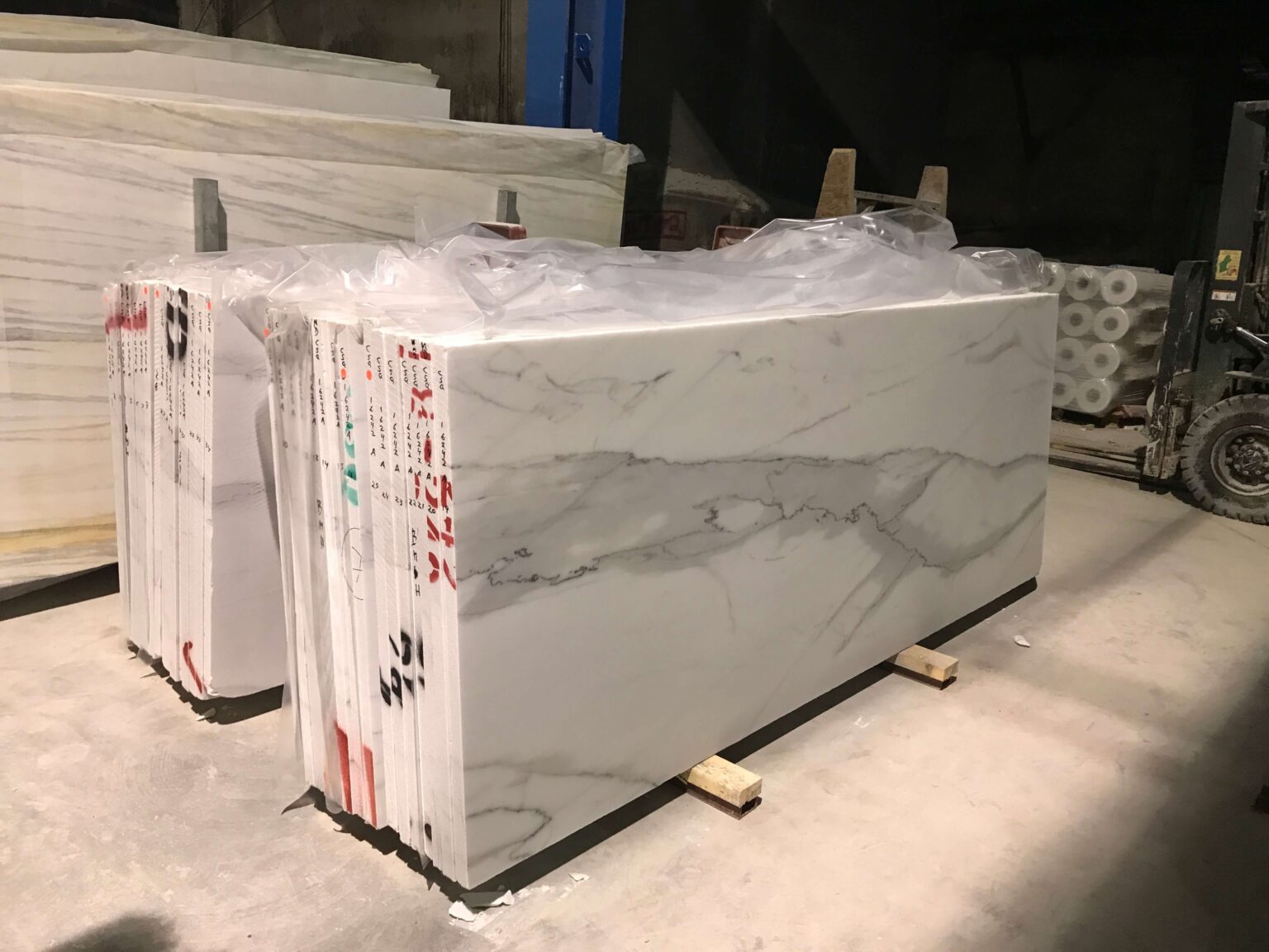 Large slabs of white marble with gray veining stacked on a pallet truck in a marble warehouse.