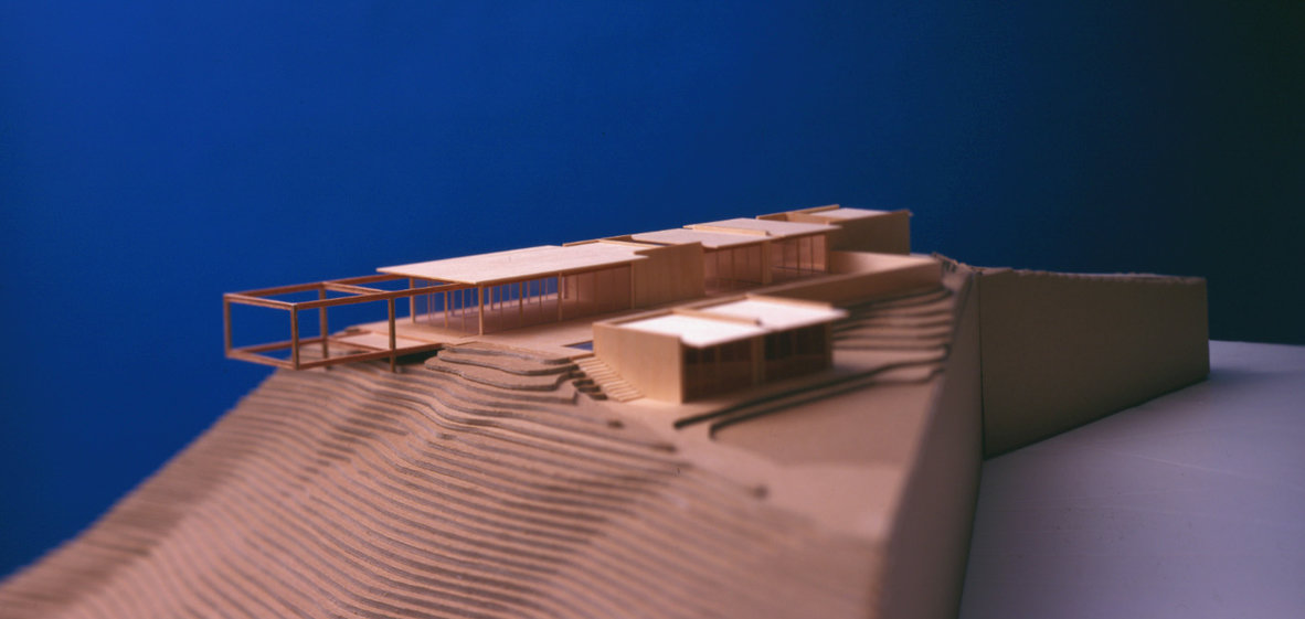 Chip board architectural model of modern desert house and topography against blue background.