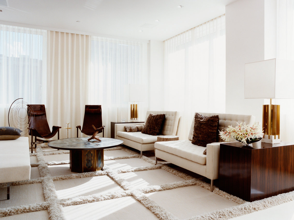 Beige and white living room with sheer curtains, upholstered sofas, and leather chairs on a large-scale grid pattern carpet.
