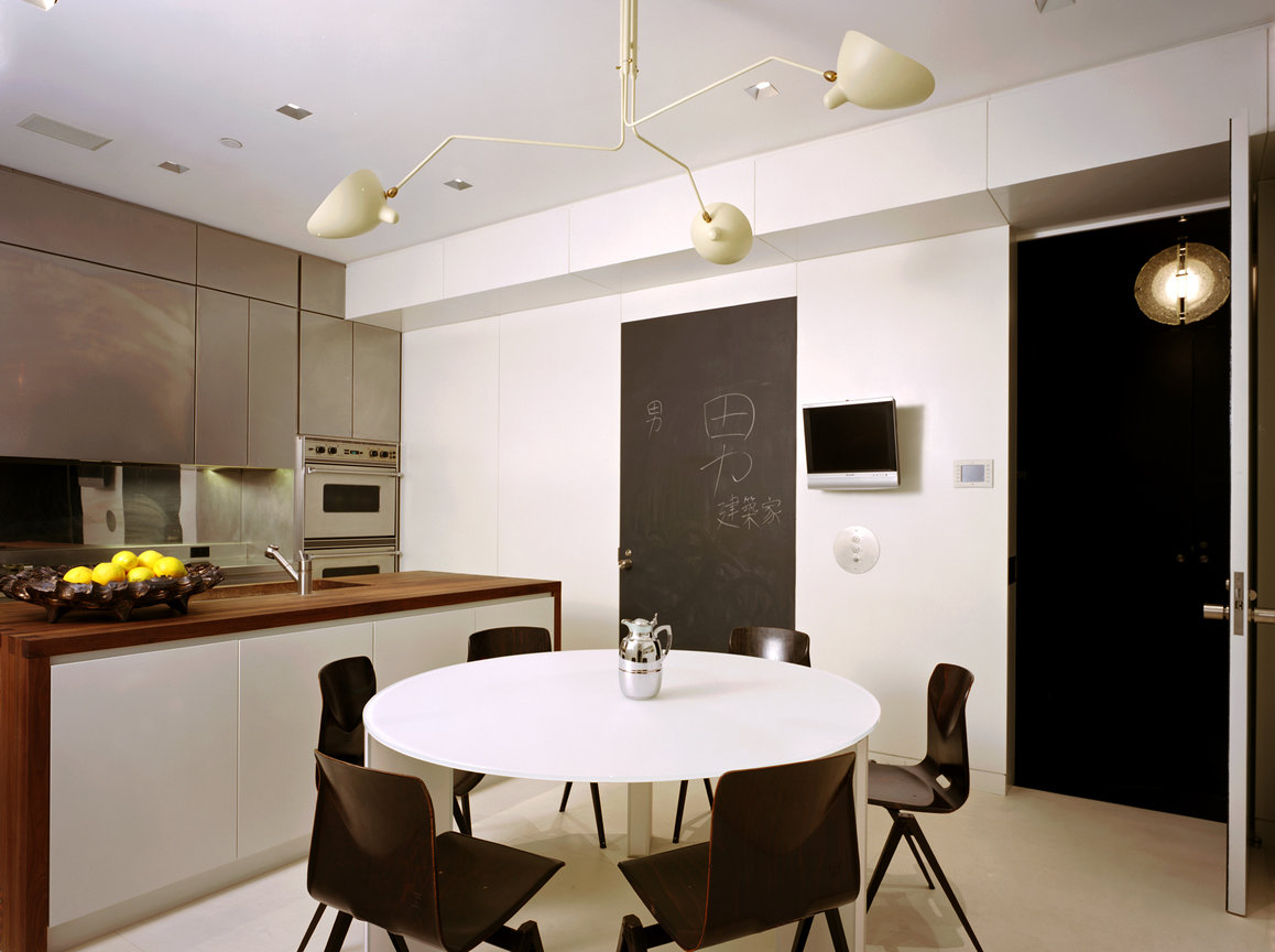 Modern kitchen with stainless steel cabinetry and appliances, dark wood counter and white round table with black chairs.