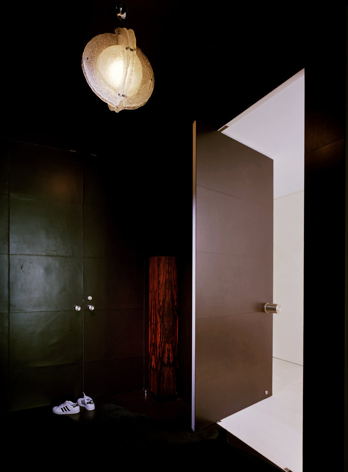 Black entry vestibule with leather panel walls, a white decorative ceiling light, and a door opening into a white interior.