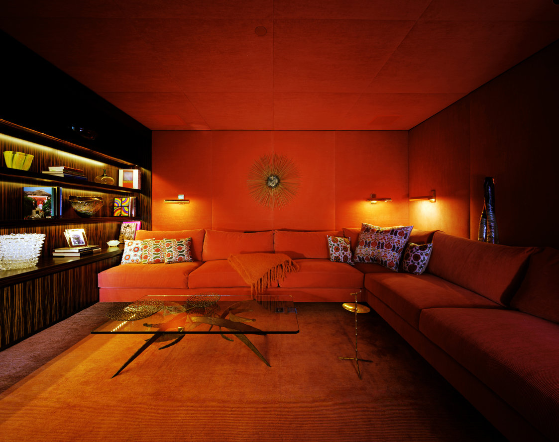 Den with red-orange corduroy sofas, walls and ceiling with matching carpet and macassar ebony millwork with display shelves.