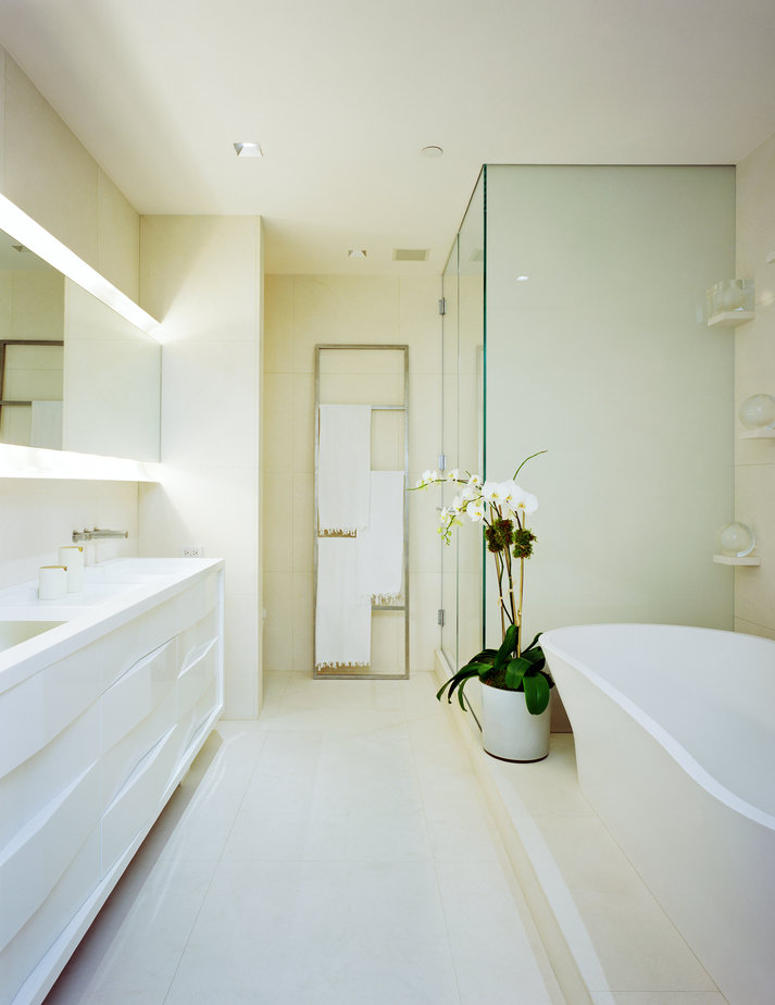 Modern, all-white bathroom with double vanity cabinet, mirror, glass shower enclosure, soaking tub and planted orchid.