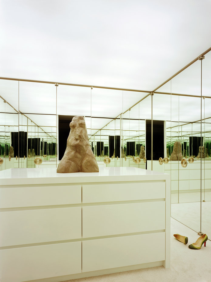Mirror-clad dressing room with white ceiling, white carpet and white lacquer island dresser and a figurative sculpture.