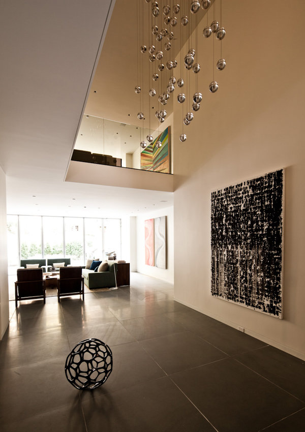 Double-height atrium of townhouse with bluestone floor, large-scale art, Bocci chandelier and living areas in background.