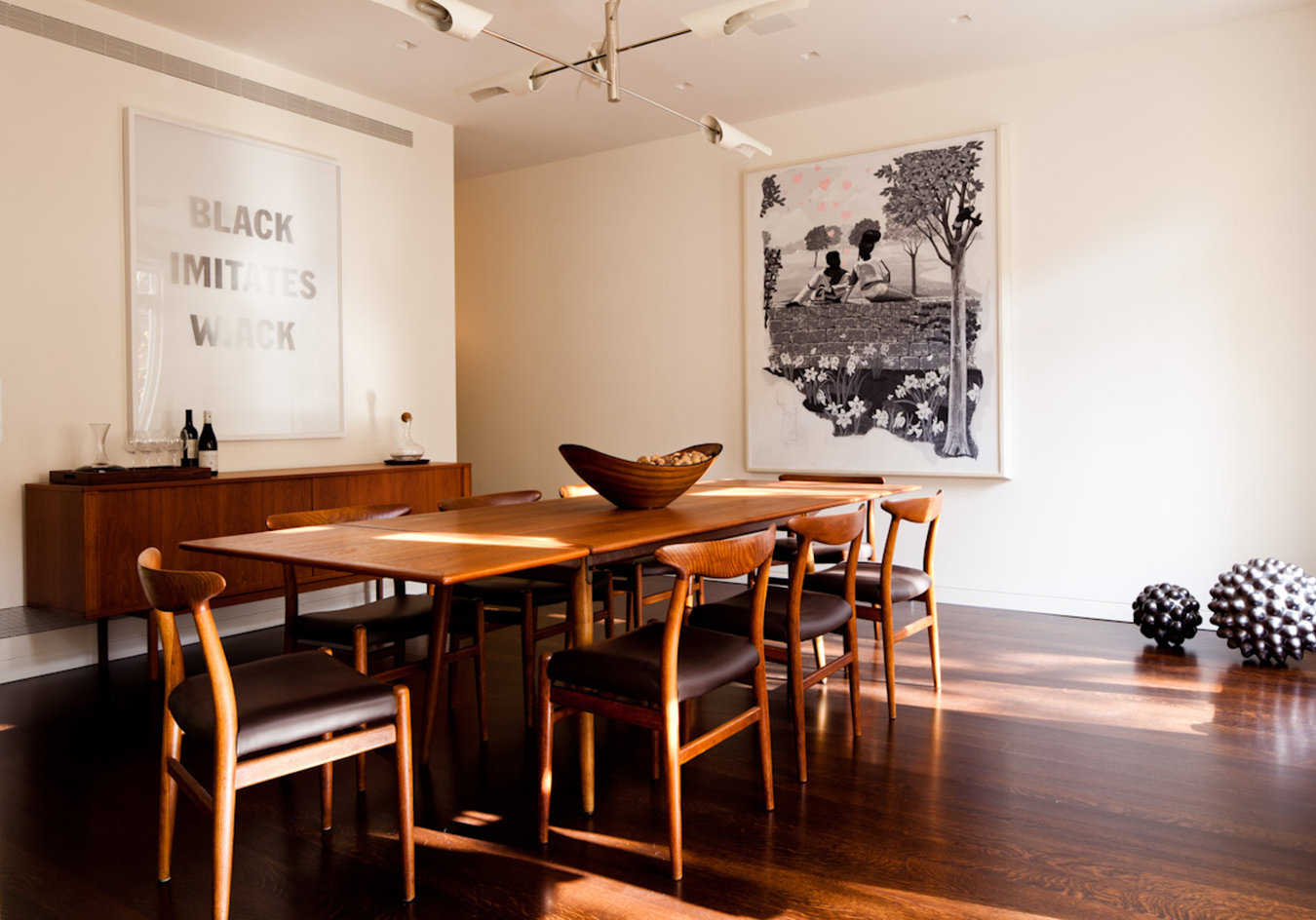 Modern dining room with midcentury wood dining table, chairs and sideboard, framed art and decorative light overhead.