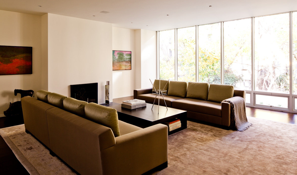 Minimalist living room with fireplace, two large sofas and wood coffee table on a silk area rug and floor-to-ceiling windows.