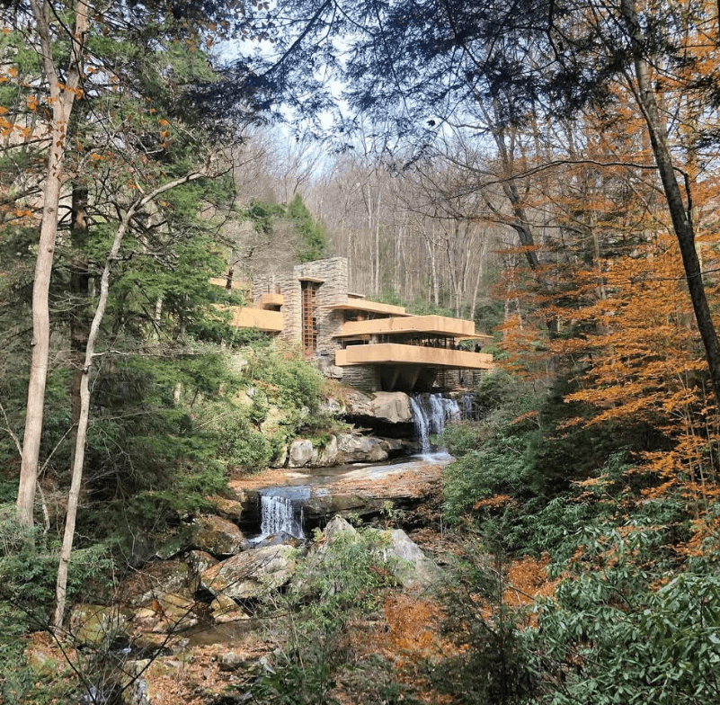 A view of Fallingwater through trees, showing a vertical structure made of quarried stone and several cantilevered terraces.
