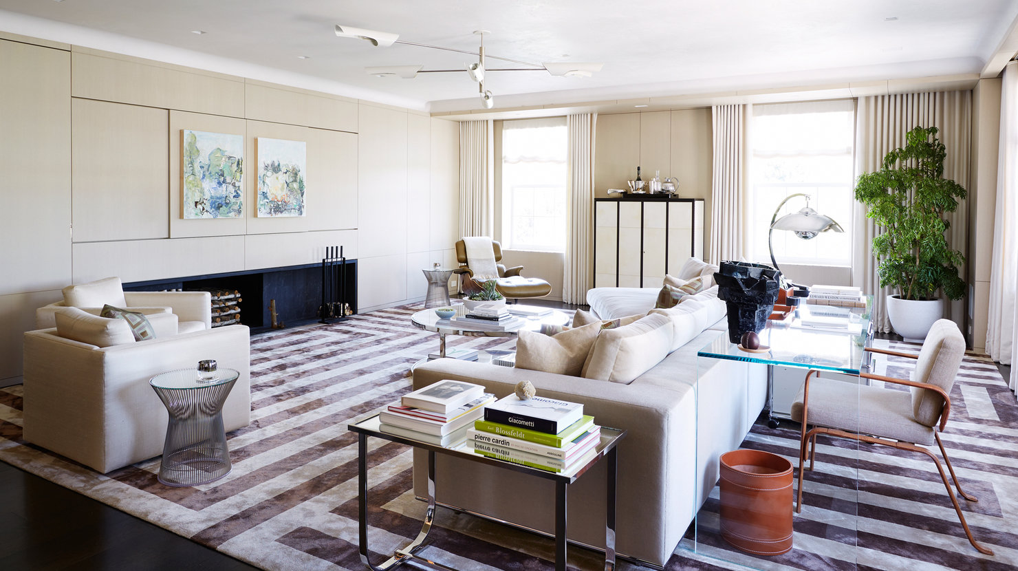 Living room in neutral palette with windows on back wall, sofa and chairs, modern fireplace, brown and beige striped carpet.