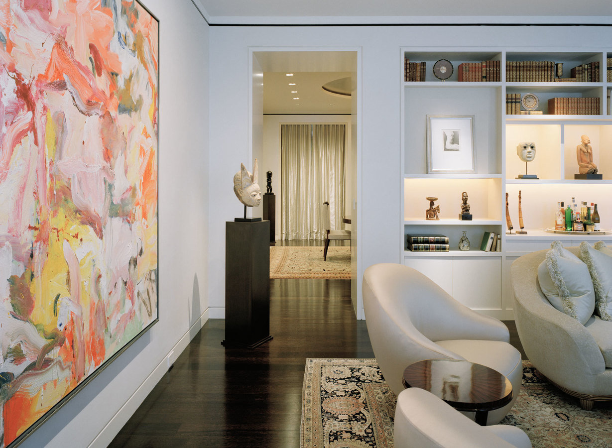 Corner of art-filled living room with abstract painting in left foreground and doorway to dining room with ivory curtain.