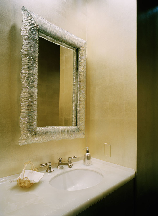 Closeup of powder room with metallic walls, decorative glass framed mirror and white onyx vanity counter with nickel faucet.