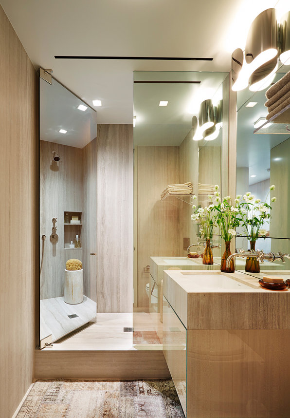 Modern bathroom in neutral palette with mirrored shower doors open to shower, stone top sink vanity and decorative sconce.