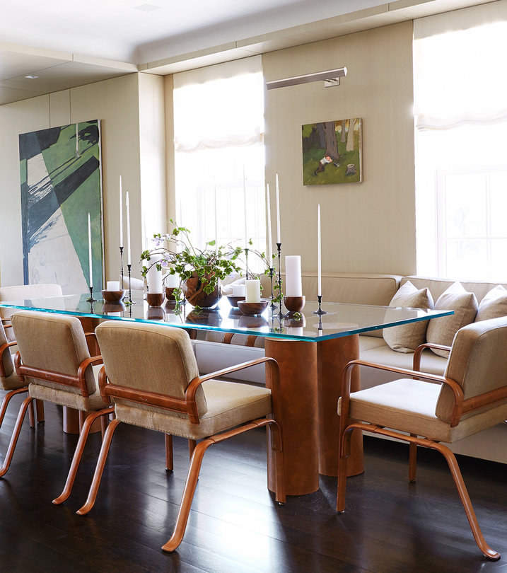 Glass top dining table with wooden double column base and coordinating chairs in wood and upholstery; beige walls and windows.