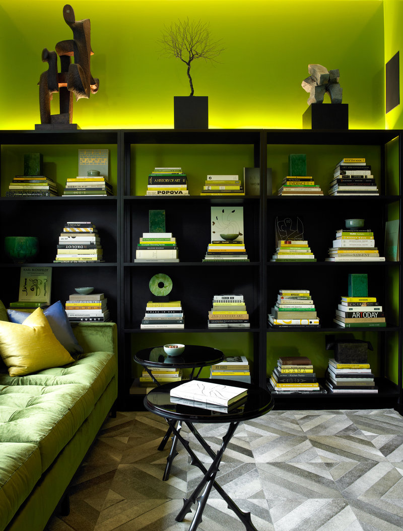 Den with acid green wall, black shelving, green velvet sofa, black end tables and a gray, hair-on-hide patterned rug.