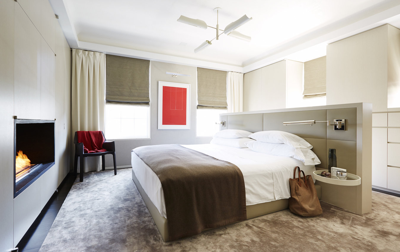 Modern bedroom with freestanding bed, beige silk carpet, millwork wall with built-in fireplace; red artwork on wall.