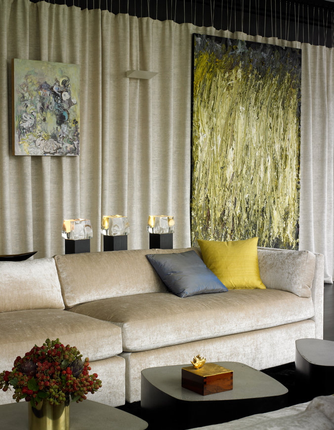 Wall of linen curtains, hanging artwork and sofa in beige velvet with throw pillows and three metal block coffee tables.