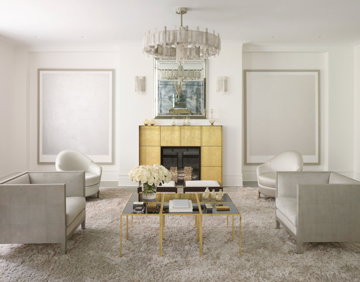 Formal living room in platinum and gold palette with fireplace and seating centered around a glass coffee table on cream rug.