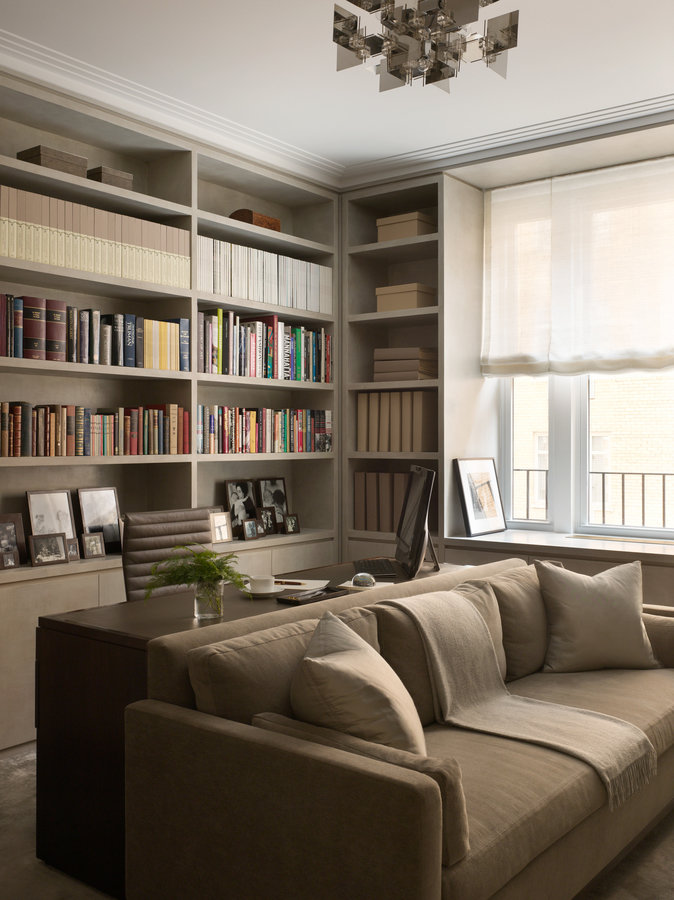 Home office in taupe color palette with a wall of bookshelves, desk and chair, sofa, modern geometric chandelier and window.