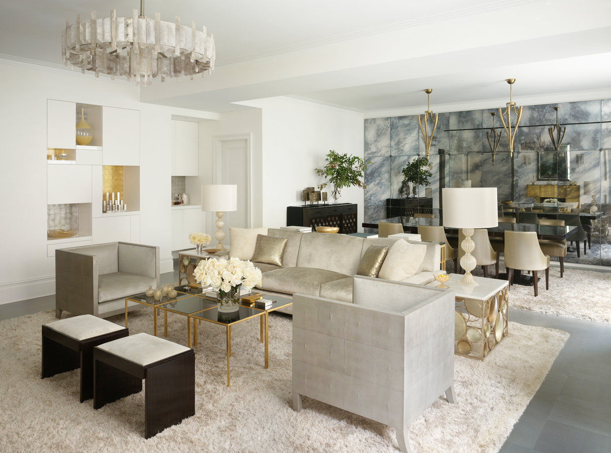 Living room with platinum colored sofa and chairs on a cream area rug, opening to formal dining room with a mirrored wall.