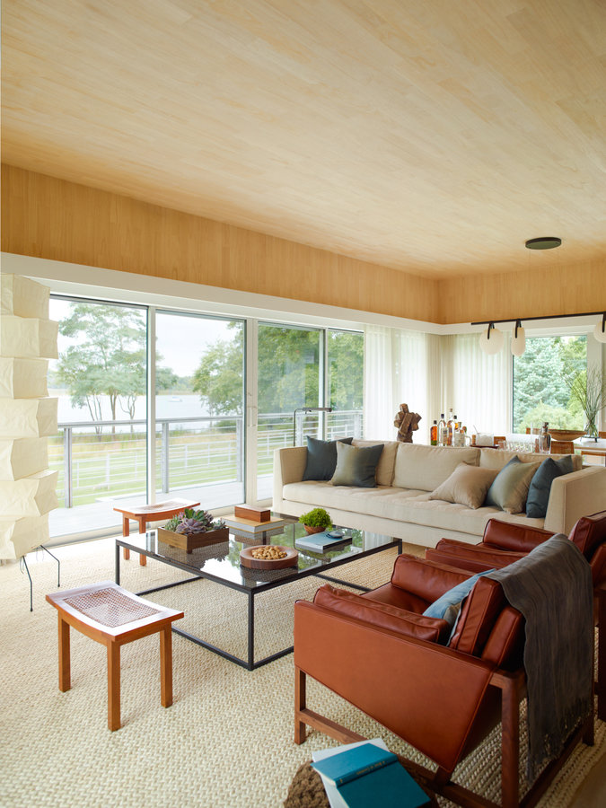 Living room with pale wood ceiling, seating arrangement with glass coffee table, standing paper lamp, sliding glass doors.