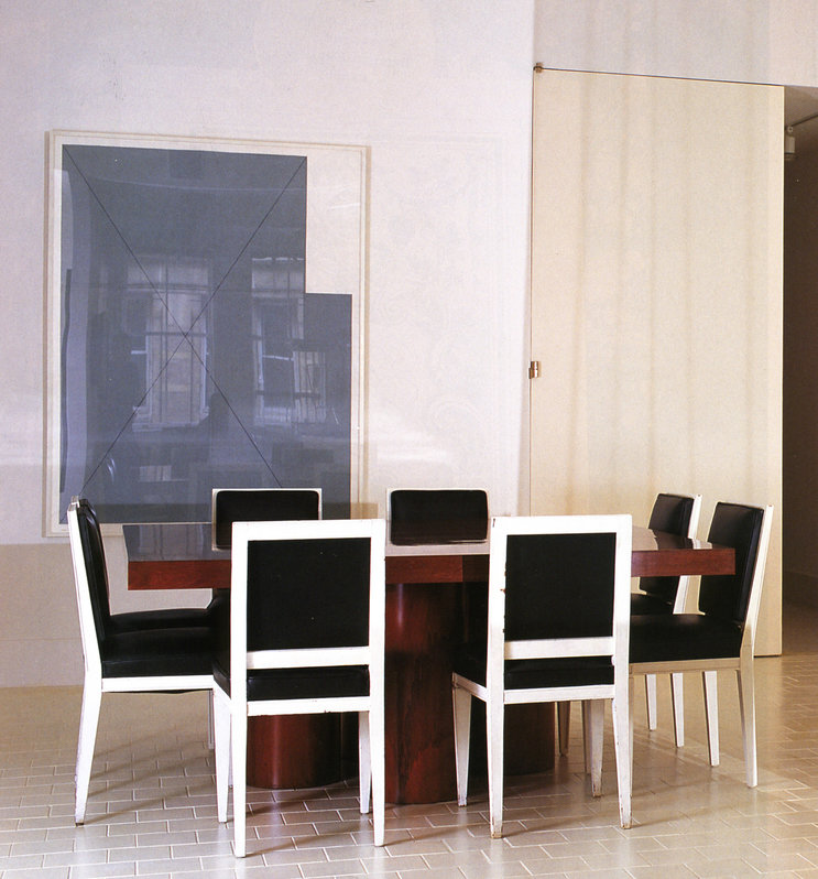 White room with white tile floor, modern, dark wood dining table with white wood and black leather chairs, art on wall.