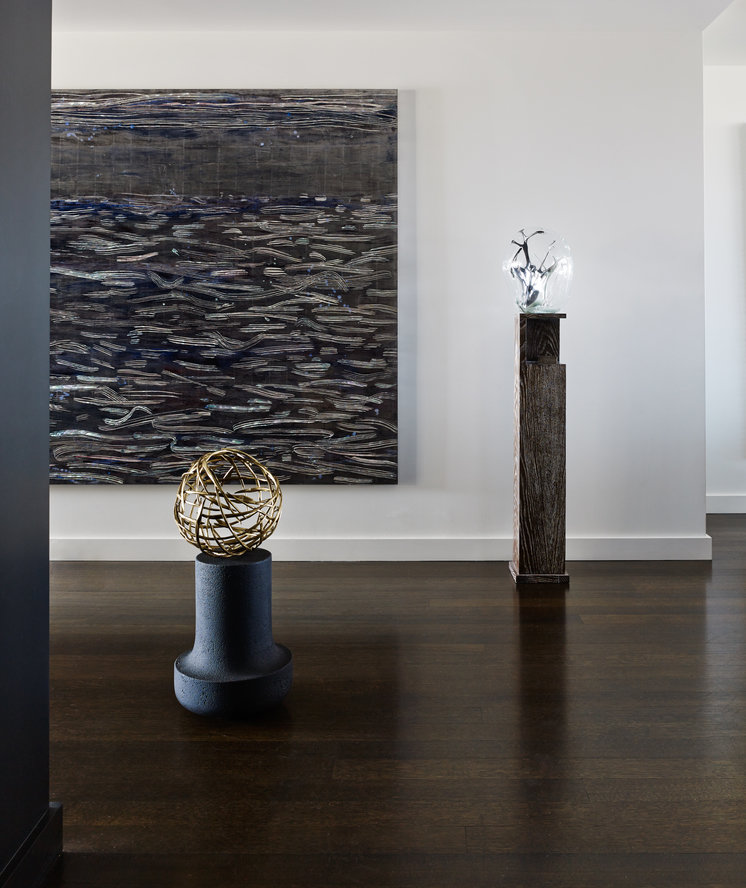 Room with white walls and dark wood floor, black abstract painting and two modern sculptures on stands.