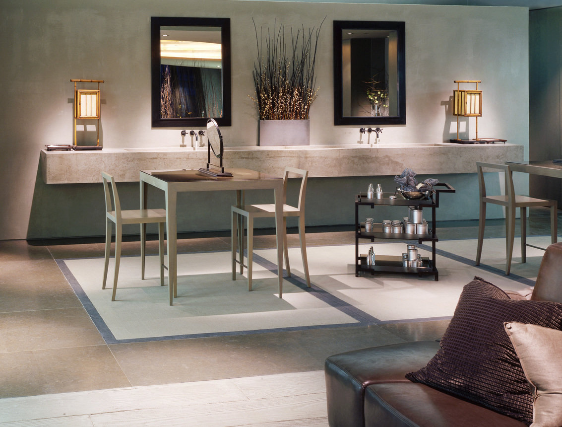 A spa area within a high-end store in a warm gray color palette. A wall-mounted sink basin, mirrors tables and seating for consultations.