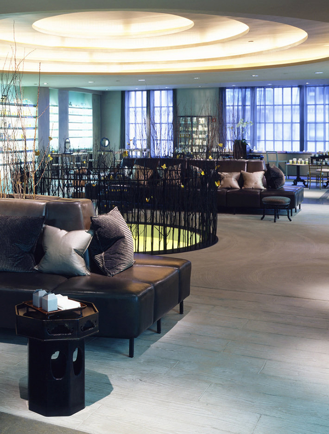 Store interior with pale wood floors, dark leather banquettes, ceiling with recessed concentric circles and windows on rear wall.