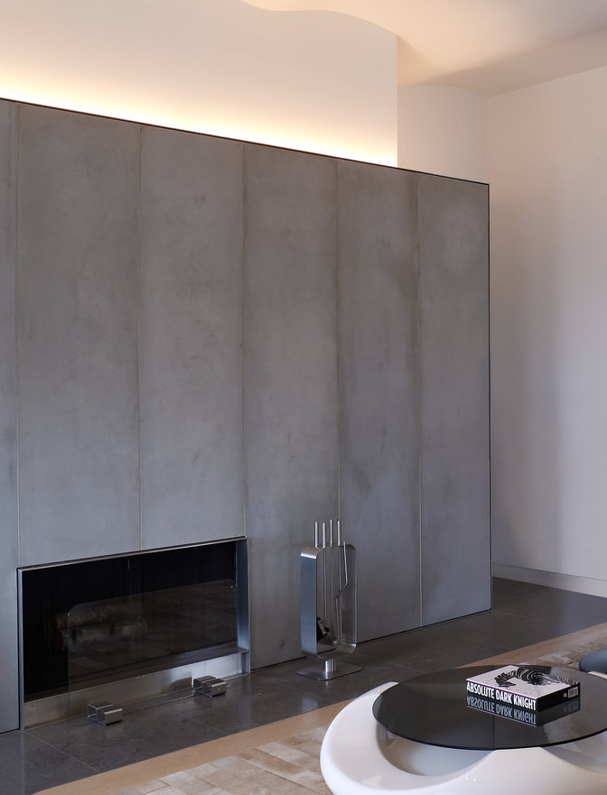 Living room with wall of lightweight glass fiber concrete panels surrounding a fireplace and coffee table in foreground.