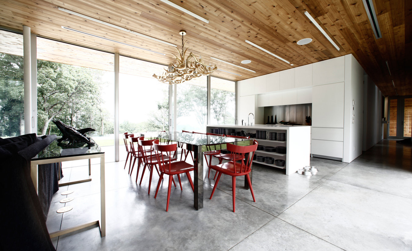 Open plan dining room and kitchen with smoked glass table and red chairs, gold antler chandelier and white lacquer kitchen.