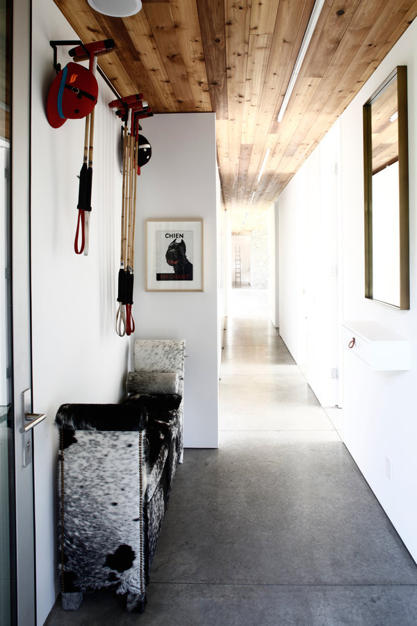 nterior corridor with white walls, cedar ceiling, concrete floor, black and white cowhide bench and polo equipment on wall.