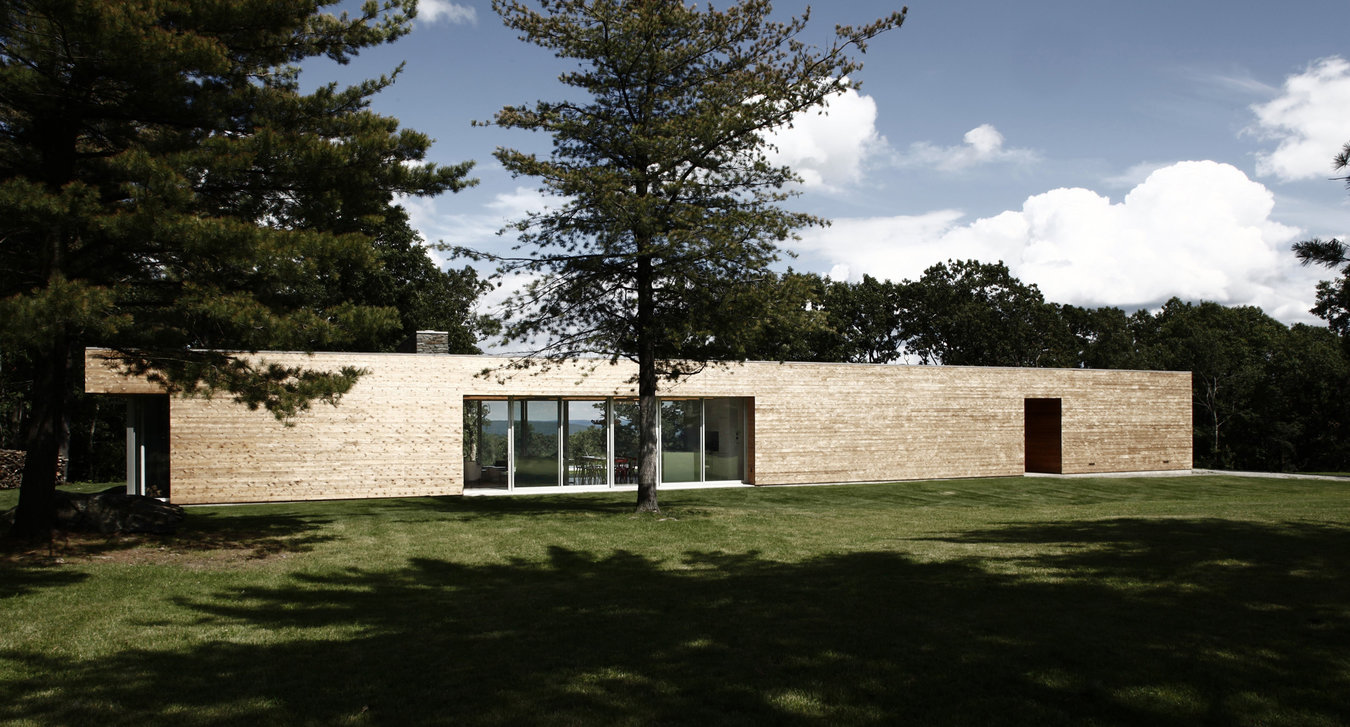 Front façade of modern, cedar-clad, bar-shaped house with front entry cutout, a large glazed span and a deconstructed end.