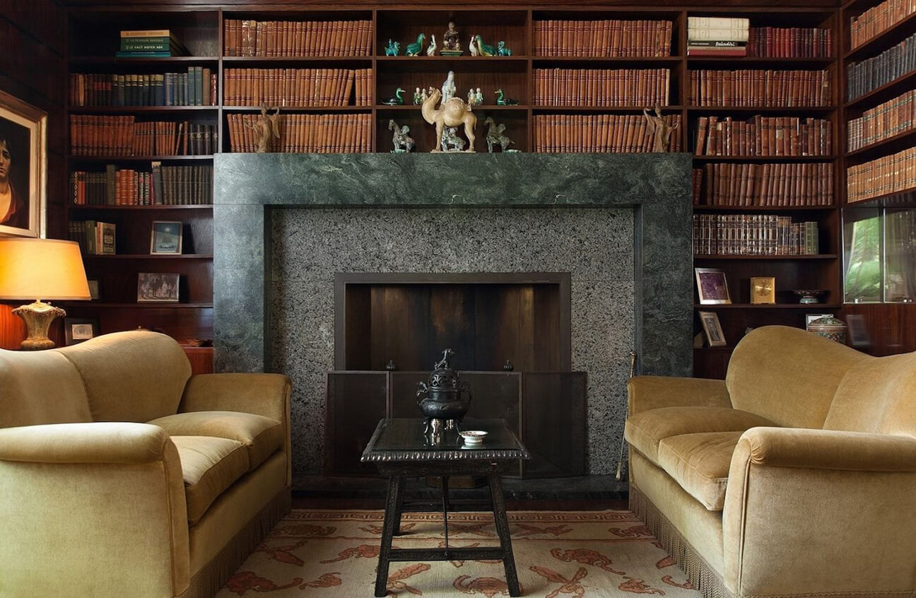 Fireplace with stone surround and a pair of facing sofas in goldenrod velvet in the library at Villa Necchi.