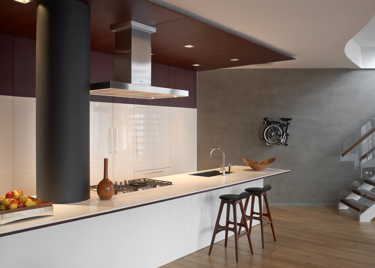 Modern kitchen with range and range hood, dark wood white lacquer cabinetry, white lacquer counter with wood stools.